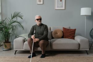 Una persona mayor ciega, sentada en un sillón con gafas oscuras puestas