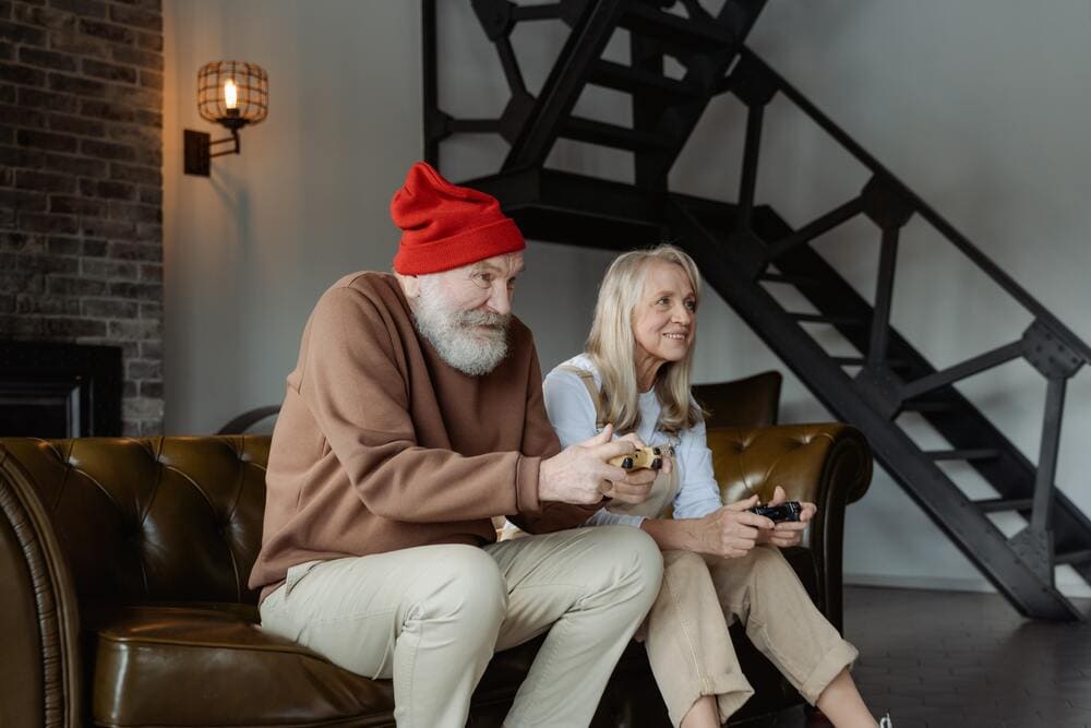 Un abuelo y una abuela jugando a la videoconsola en el sofá de su casa