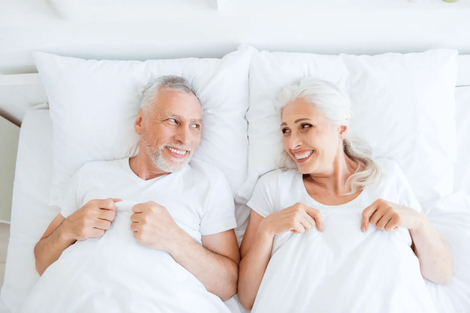 Dos ancianos se ríen en la cama mientras se miran el uno al otro. 
