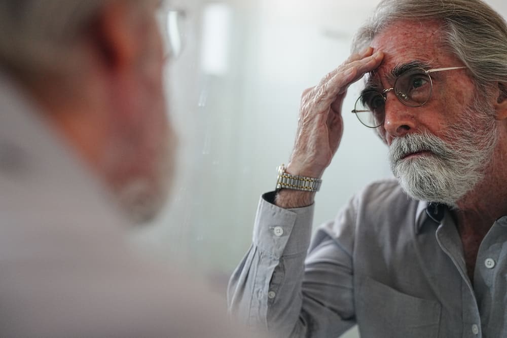 Un señor mayor se mira en el espejo mientras se toca el pelo. 