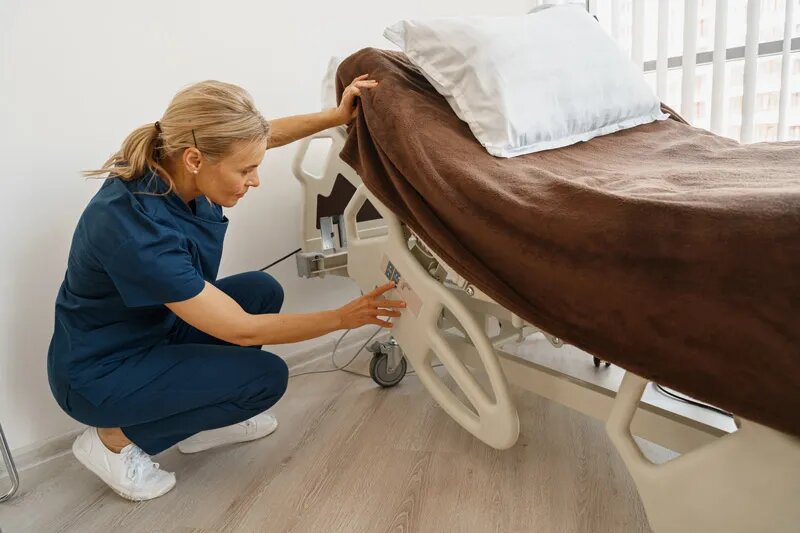 Una cuidadora prepara una cama articulada preparada para llevar a cabo la posición Fowler, de manera inclinada.