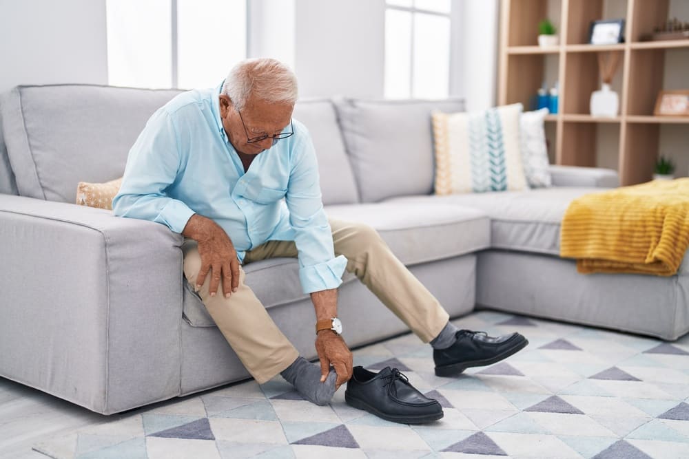 Un hombre mayor se duele de unas ampollas en los pies en el sofá de su casa. 