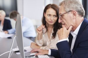 Una mujer adulta enseña algo a un señor mayor en una empresa a través del portátil.