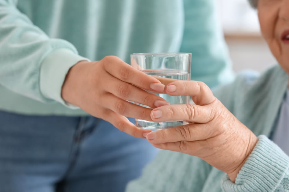 Un señor mayor le ofrece un vaso de agua a su mujer. 
