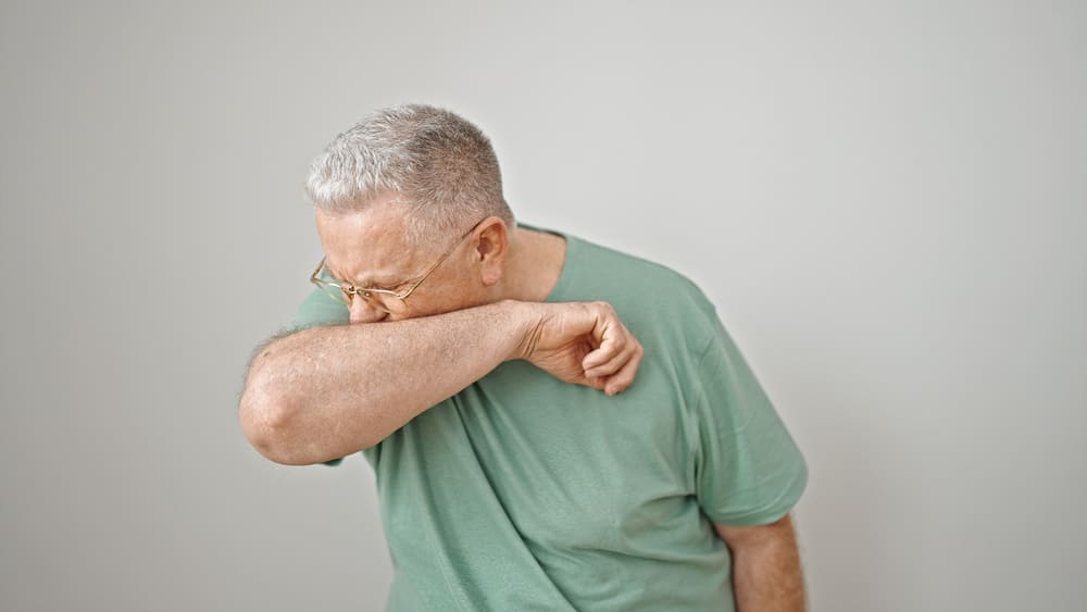 Un hombre mayor se tapa la boca con el brazo mientras estornuda. 