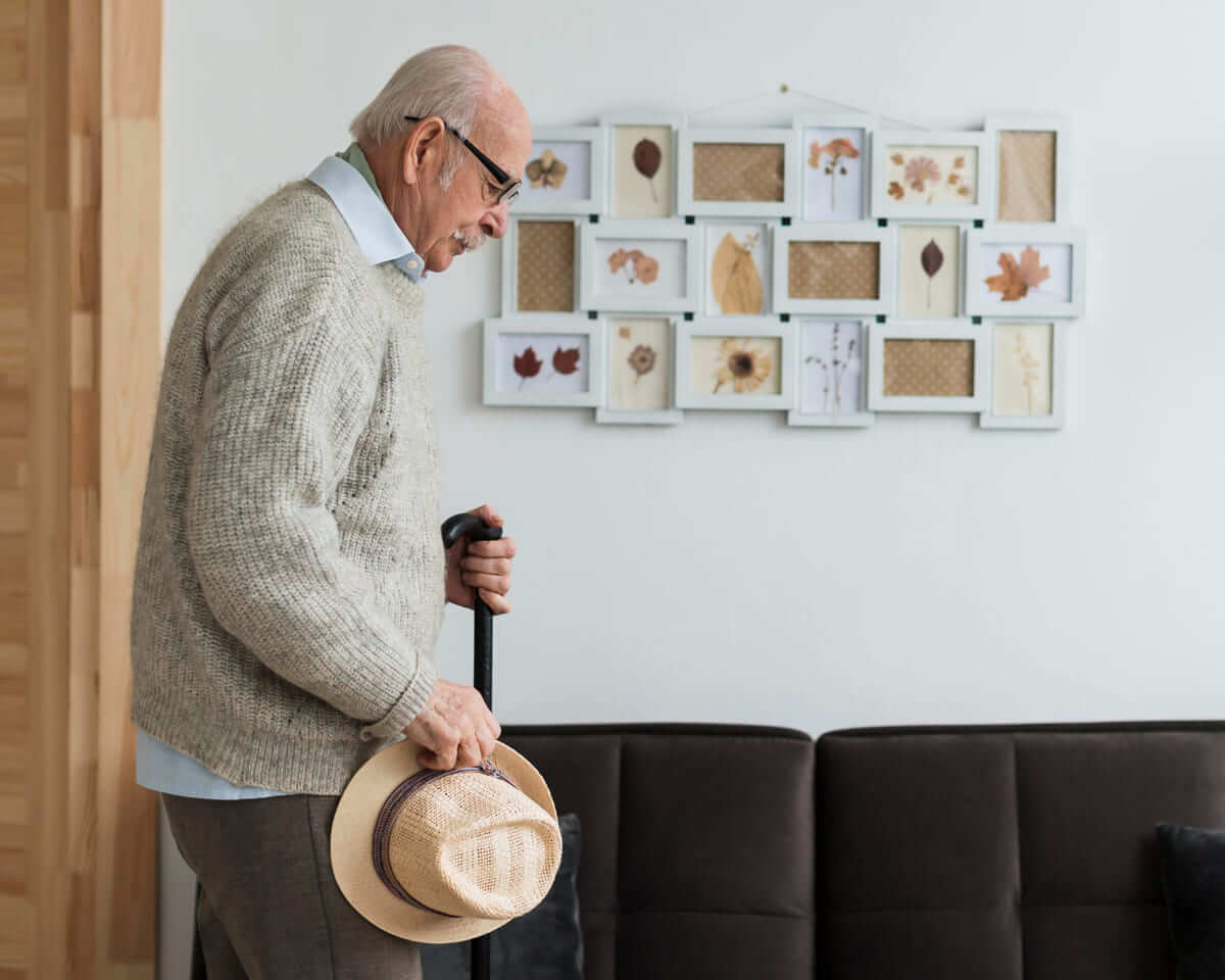 Un anciano con un bastón y un sombrero en la mano.