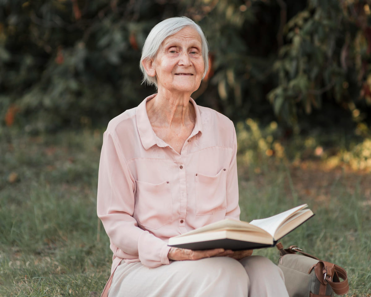 Una anciana leyendo un libro al aire libre.