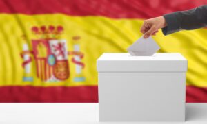 Una persona poniendo su voto en la urna con una bandera de España de fondo.
