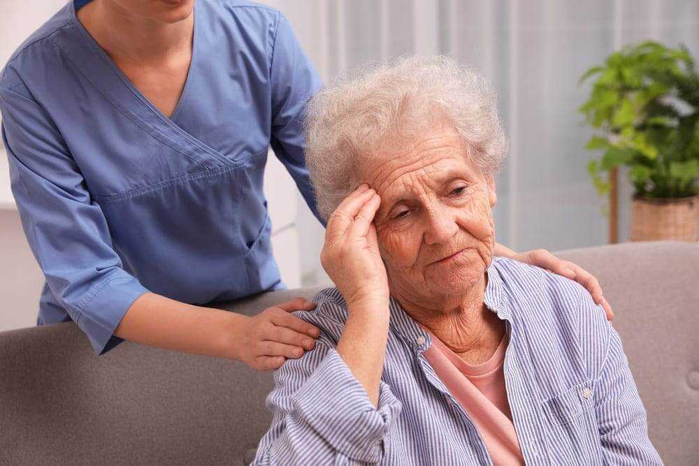 Una cuidadora apoya a una mujer mayor en el sofá de su casa. 
