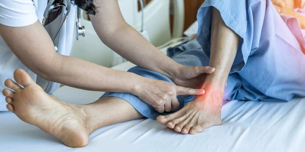 Una cuidadora señala la zona del tobillo de una persona mayor que está afectada. 