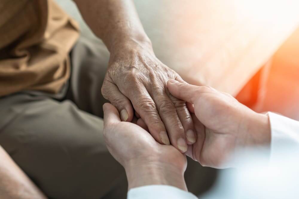 Un plano detalle de unas manos de una psicóloga cogiendo la mano izquierda de una persona mayor. 