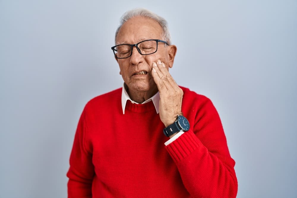 Un anciano se duele de la mejilla mientras se palpa con su mano. 