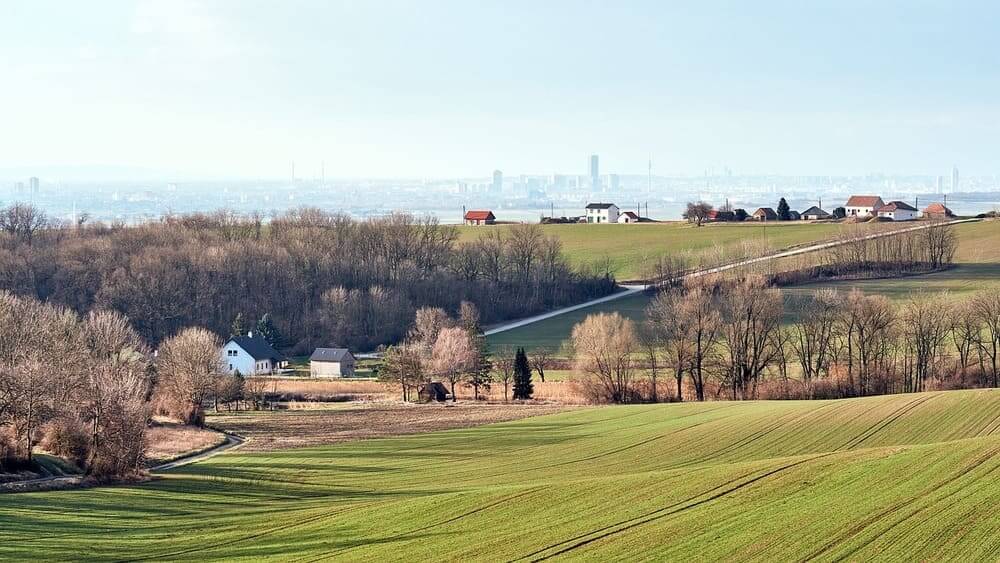 Una imagen que muestra el contraste entre una zona rural verde alejada de la ciudad y al fondo una gran ciudad. 