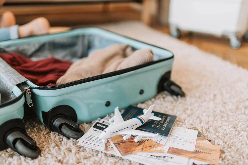 Una maleta abierta con ropa, documentos y el pasaporte al lado. 