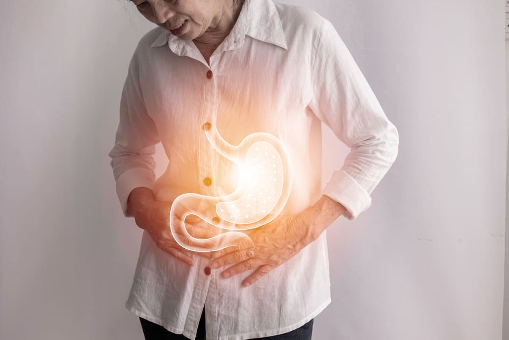 Una imagen de una anciana quejándose de un dolor del estómago mientras el aparato digestivo está representado en 3D. 