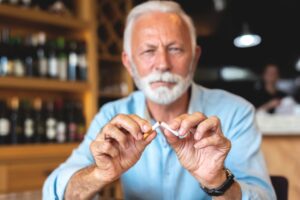 Un hombre mayor de 65 años rompe un cigarrillo por la mitad.