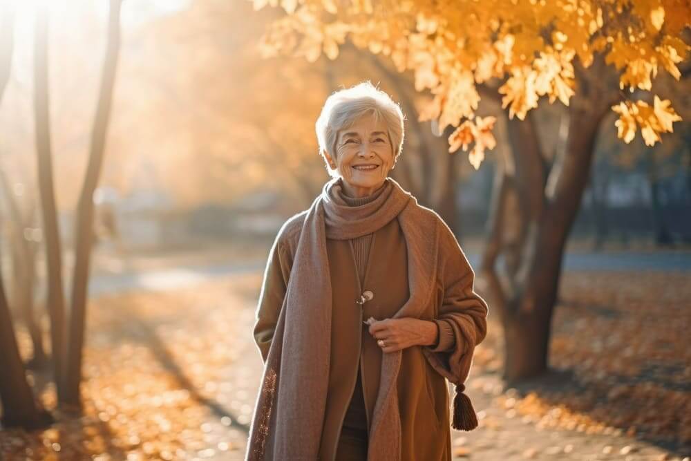 Una mujer mayor sonríe mientras camina por un parque con ropa de otoño. 