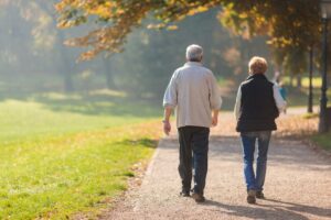 Una pareja de ancianos camina en otoño por un camino de una zona verde.