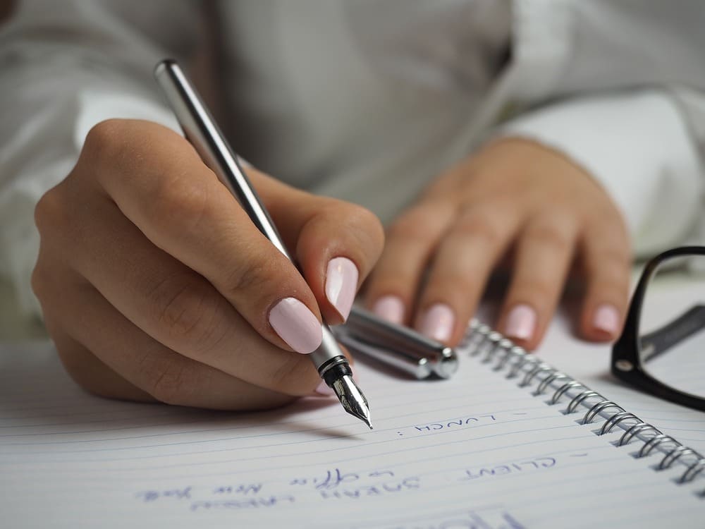 Unas manos de una chica sosteniendo un bolígrafo y haciendo apuntes en una libreta. 