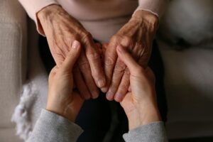 Unas manos de una cuidadora cogen a las de una anciana.