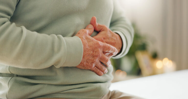 Una señora mayor se queja de un dolor de estómago con las manos reposadas sobre él.