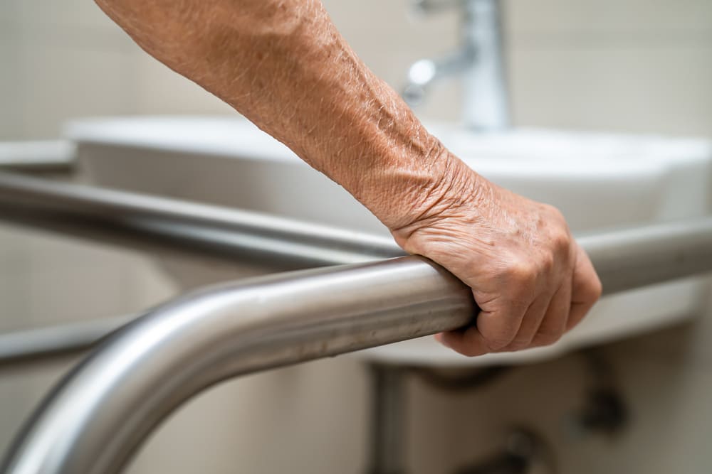 Un brazo de una persona mayor sujetándose en una barra de su baño mientras se dispone a orinar. 
