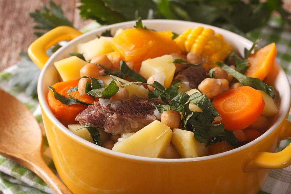 Un puchero andaluz con los ingredientes, la carne, las patatas, la zanahoria en una olla. 