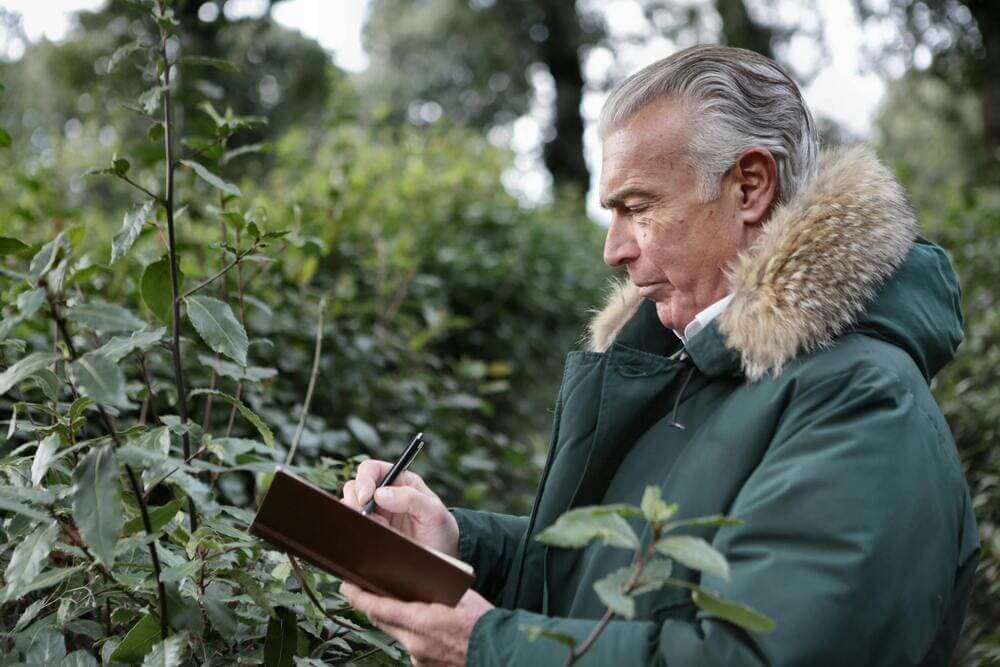 Un anciano apunta unas notas en un cuaderno en mitad de un parque. 