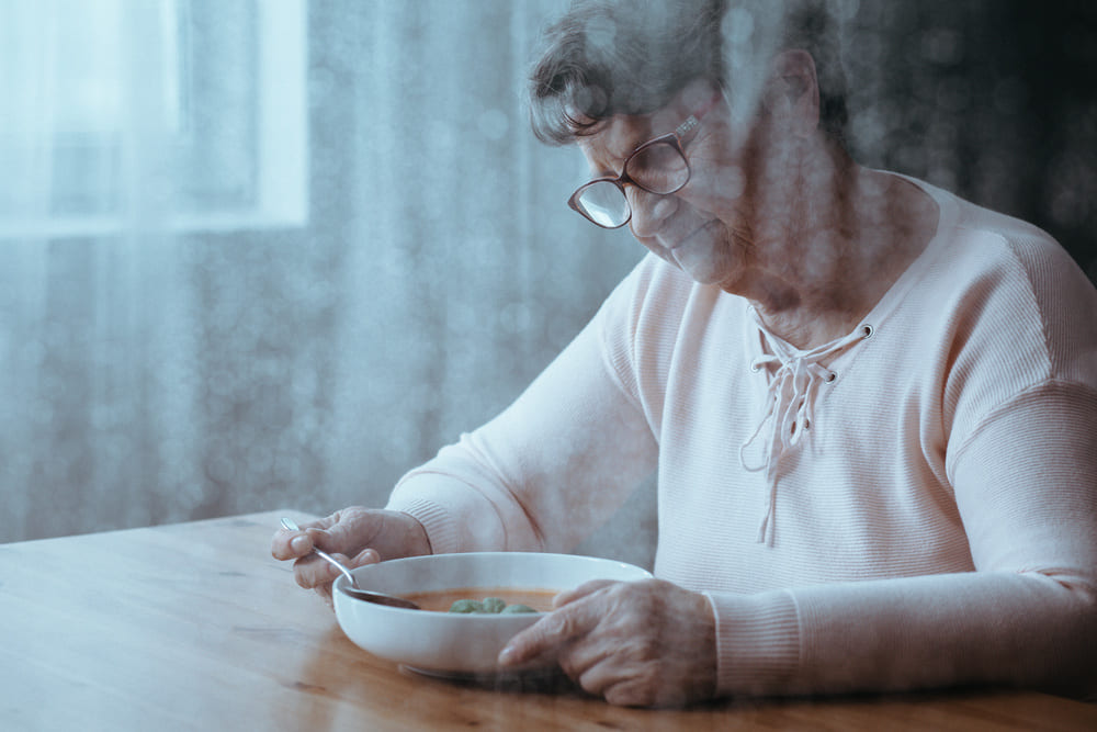Una anciana mira un plato de sopa con desgana sentada. 