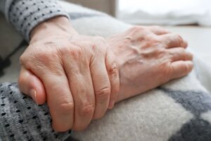 Un plano detalle de unas manos de una cuidadora agarrando a las de una señora mayor.