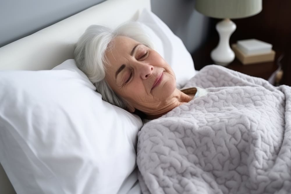 Una anciana reposa boca arriba en su cama mientras duerme. 