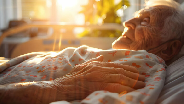 Un anciano tumbado boca arriba en la cama mientras una mano se posa sobre él.