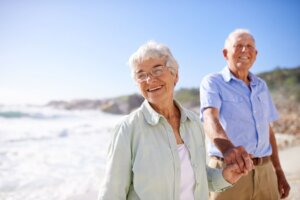 Dos ancianos sonríen mientras camina por la orilla de la playa.