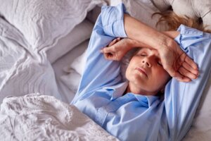 Una señora mayor en la cama con los brazos cruzados en la frente aquejada por el calor.