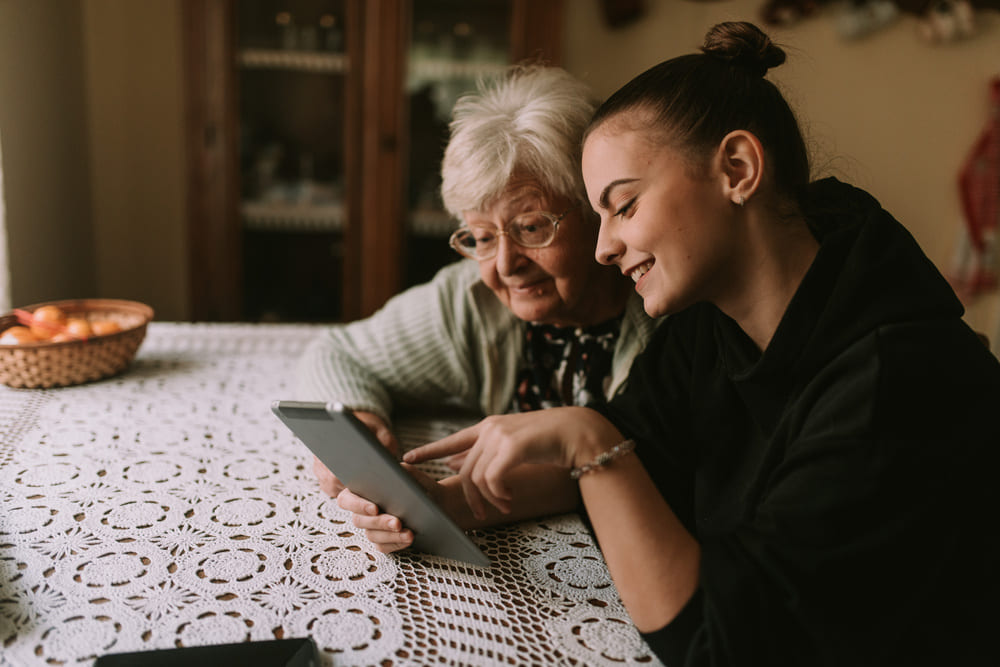 Una chica joven enseña en la tablet algo divertido a una anciana. 