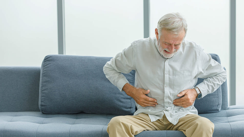 Un anciano se queja en el sofá de su casa de un dolor abdominal. 