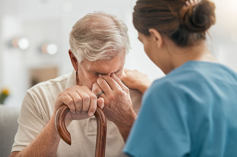 Una cuidadora consuela a un anciano que porta un bastón y que está llorando. 