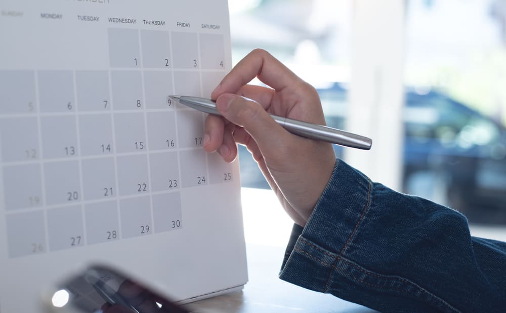 Una mano de una mujer con un bolígrafo dibuja algo en un calendario. 