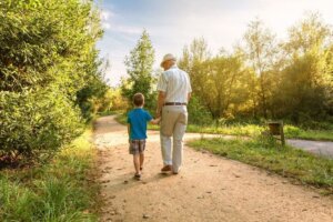 Un anciano pasea con su nieto cogidos de la mano por un campo.