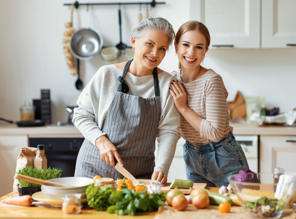 Una cuidadora y una señora mayor cocinan alegres en una cocina. 