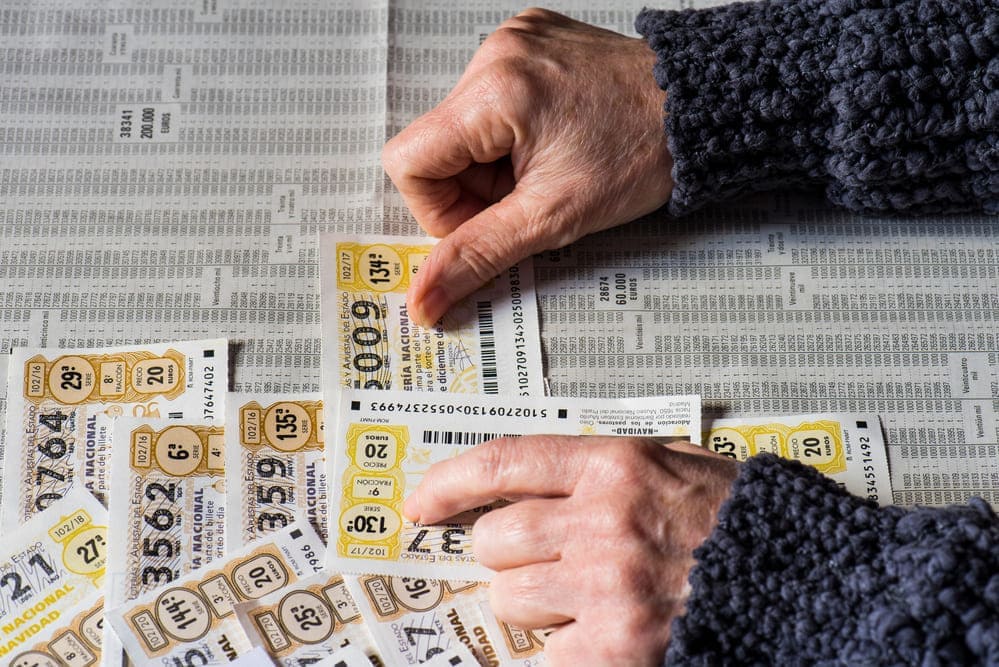 Unas manos de un anciano junto a una mesa con décimos de lotería. 