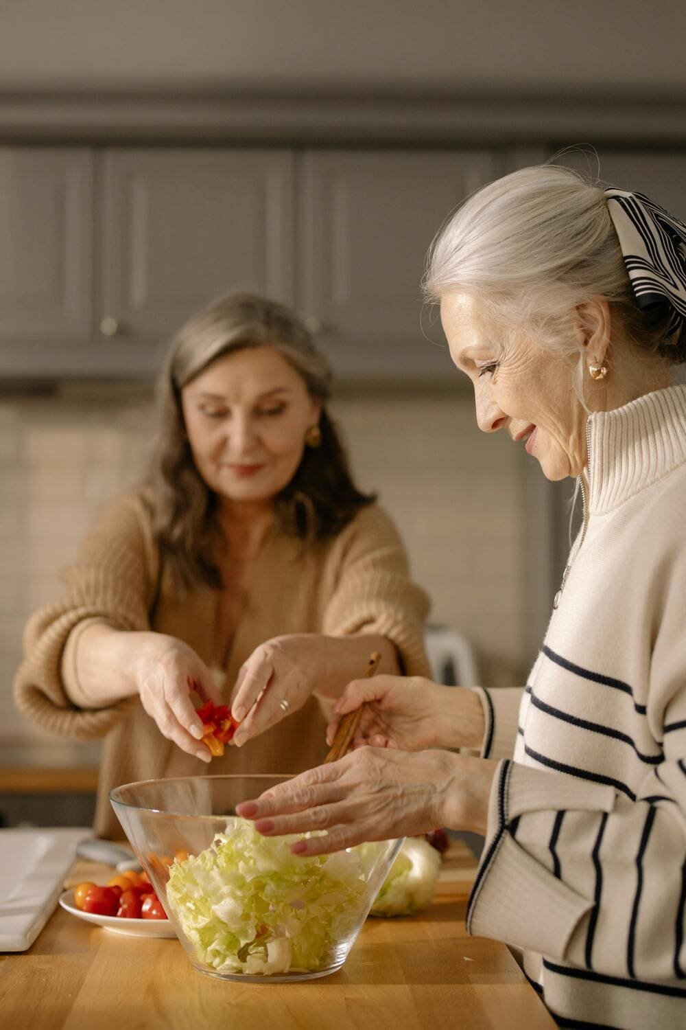 Dos mujeres mayores preparan una ensalada en una casa. 