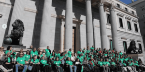 Un grupo de personas con camisetas verdes simbolizando a la enfermedad de la ELA junto a la puerta del Congreso de los Diputados.