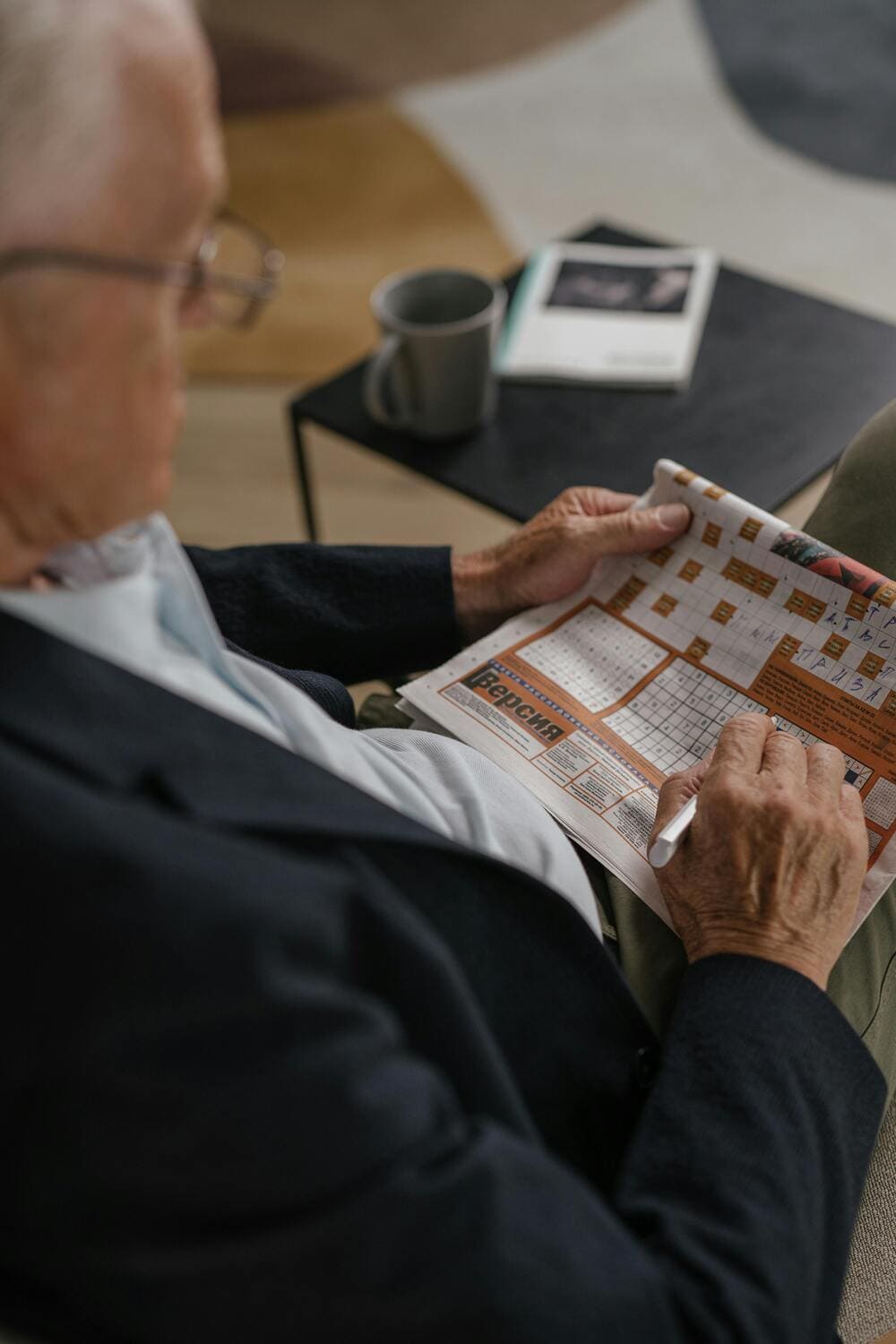 Un señor mayor con gafas se encuentra en su casa jugando a descifrar un sudoku. 