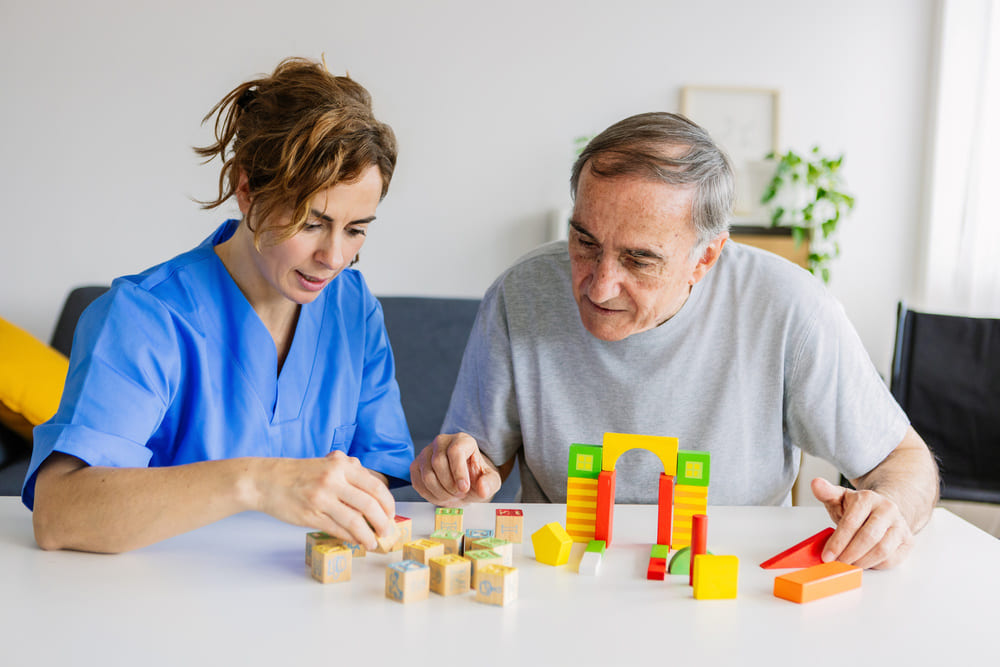 Una animadora sociocultural ayuda a un señor mayor a crear un puzzle. 