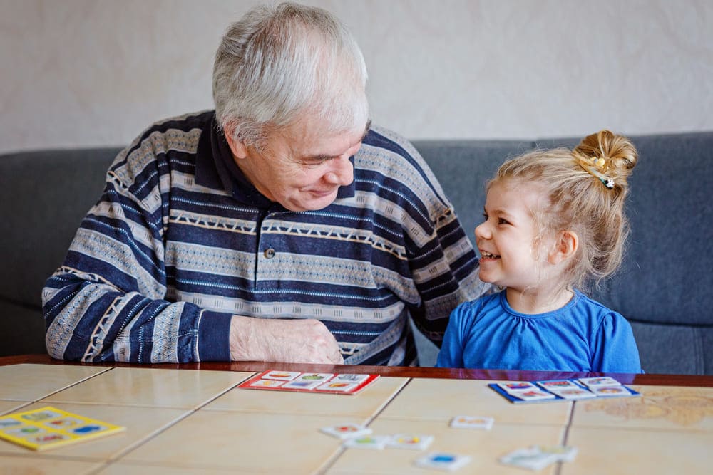 Un abuelo sonríe y juega con su nieta en una casa. 