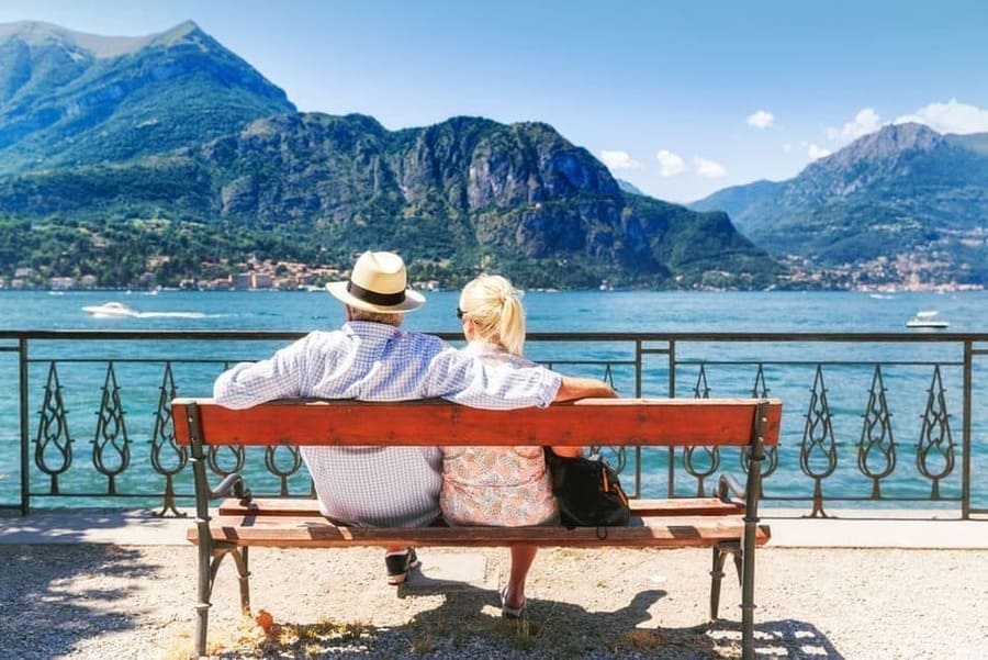 Una pareja de jubilados de espaldas sentados en un banco mirando al mar. 