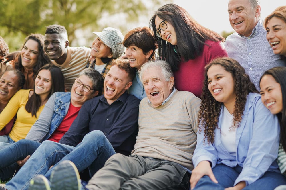 Un grupo de jóvenes y mayores sonrién todos juntos al aire libre. 