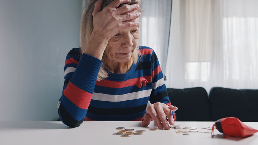Una mujer mayor cuenta su poco dinero en un monedero en su casa. 