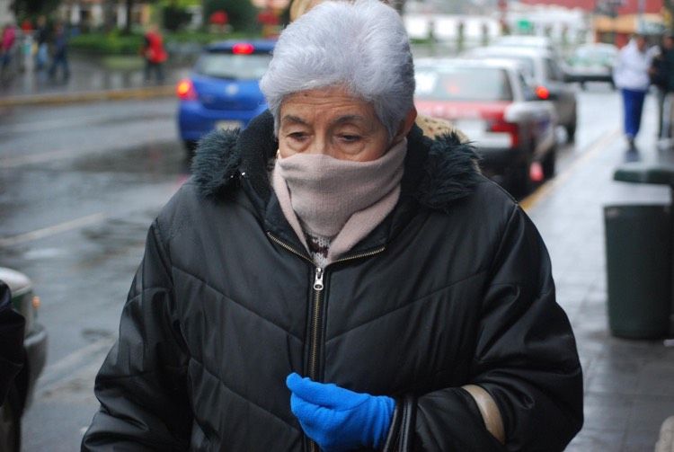 Mujer mayor con guantes, abrigo y bufanda tapándose la boca y garganta para protegerse del frío 